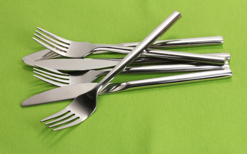 Brand new silverware, forks and knives, on a green tablecloth.